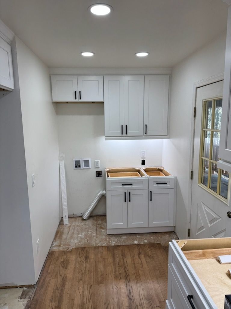 White laundry room with cabinets, sink base, and a door, under construction.
