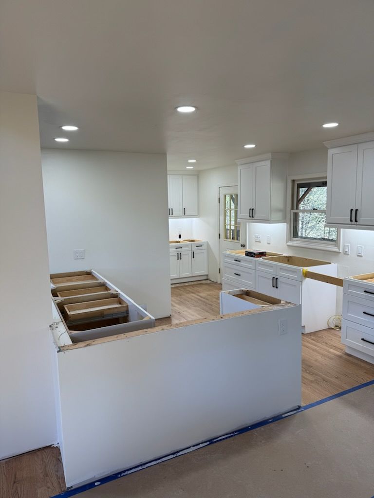 Kitchen under construction: white cabinets, countertops, and appliances. New drywall, recessed lighting.