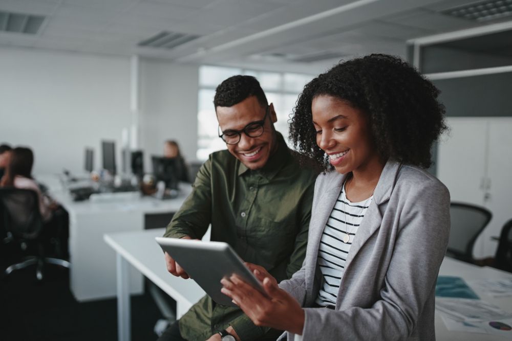 A man and a woman are looking at a tablet in an office.