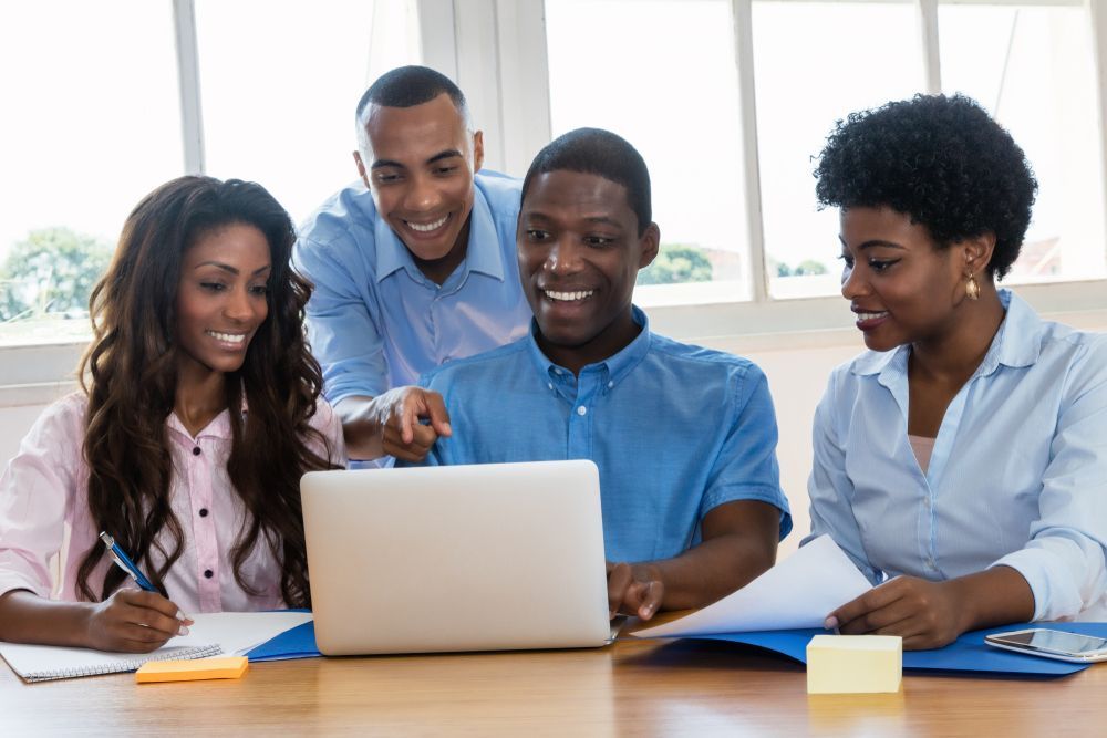 A group of people are sitting at a table looking at a laptop computer.