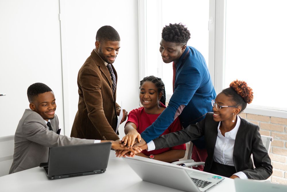 A group of people are putting their hands together in front of a laptop computer.