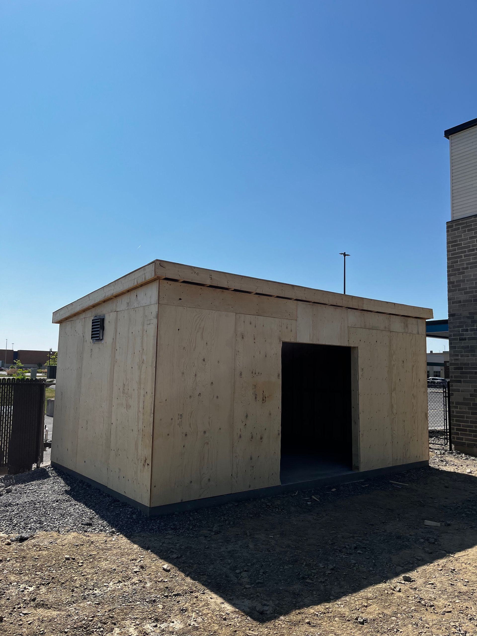 Un petit hangar en bois se trouve au milieu d'une zone de gravier.