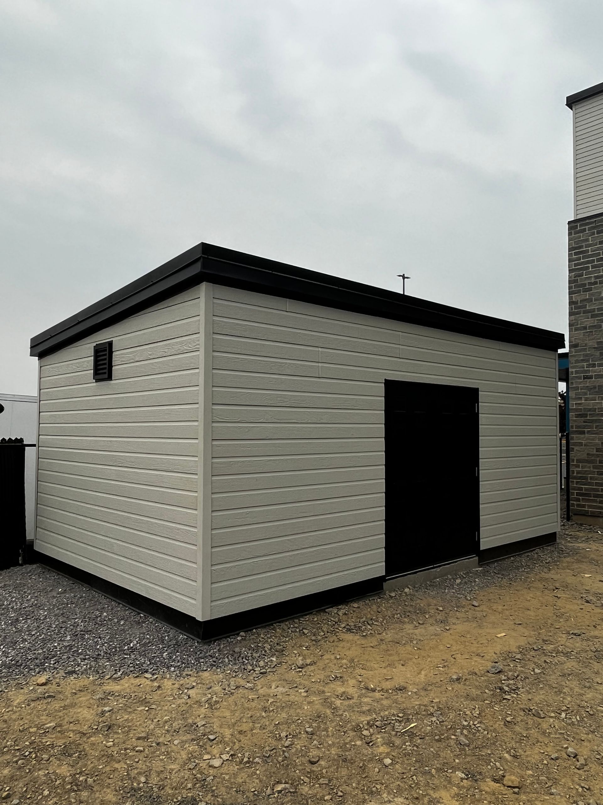 Un petit bâtiment blanc avec un toit noir se trouve au sommet d'un champ de terre.