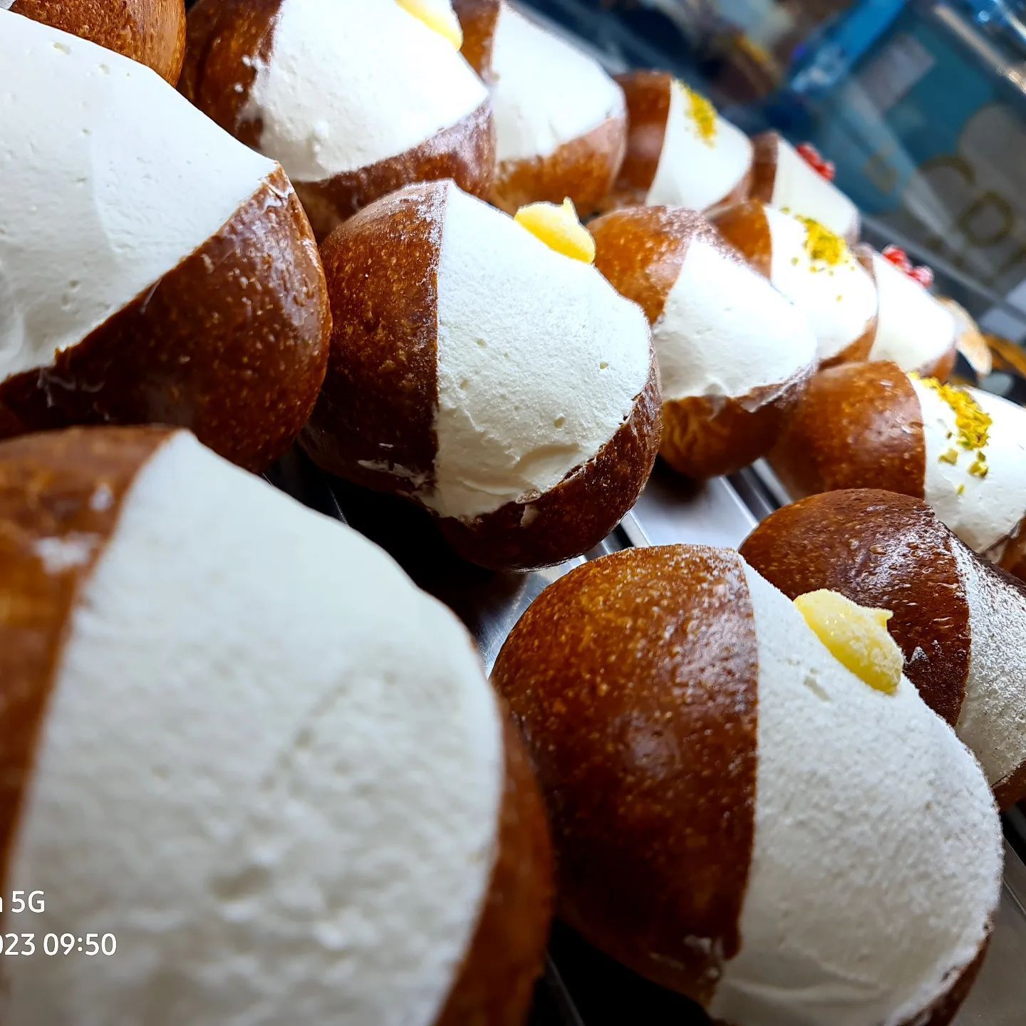 File di pasticcini rotondi, ricoperti per metà di crema bianca, esposti in una vetrina da pasticceria.