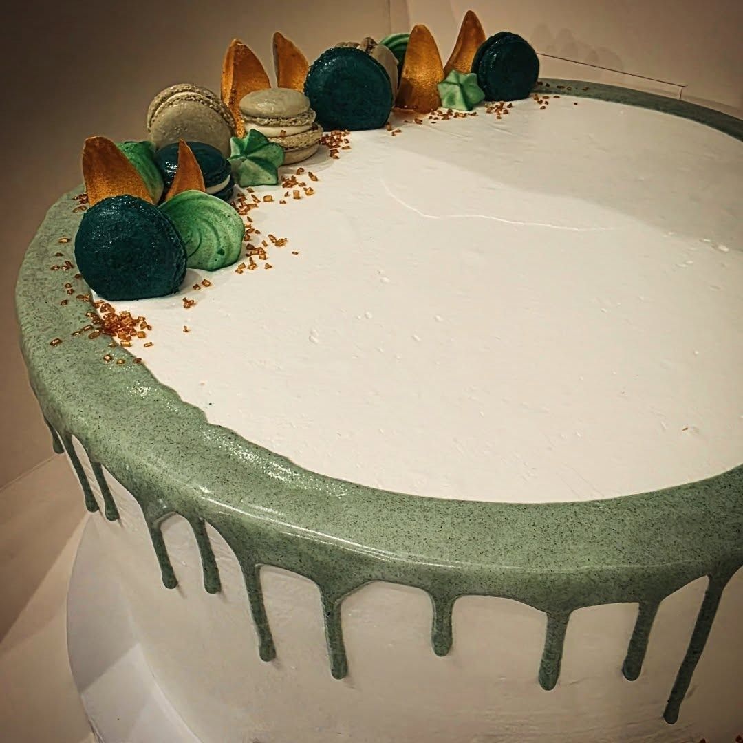 Torta bianca con glassa verde, guarnita con macaron e decorazioni in foglia d'oro.