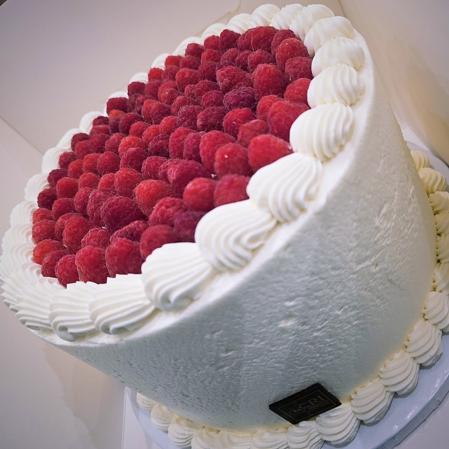 Torta glassata bianca con lamponi e riccioli di panna.