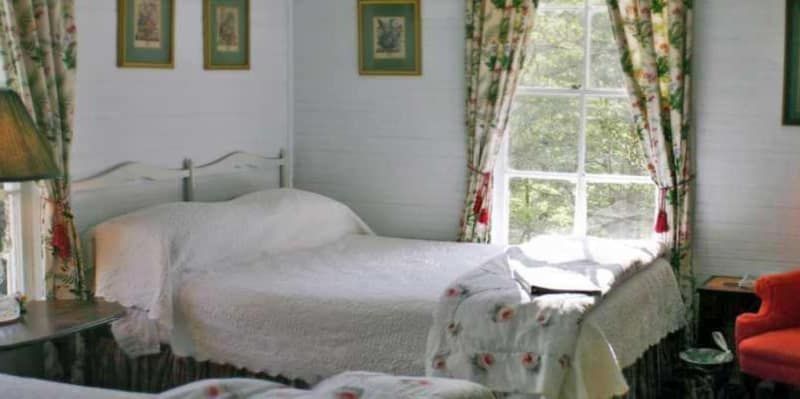 A bedroom with two beds , a chair , a lamp and a window.