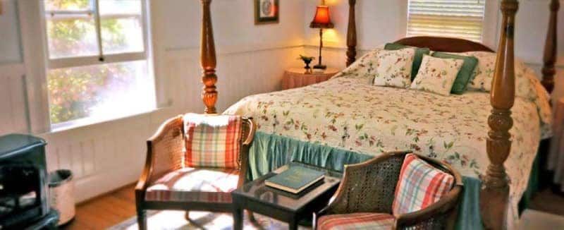 A bedroom with a four poster bed , chair , table and stove.