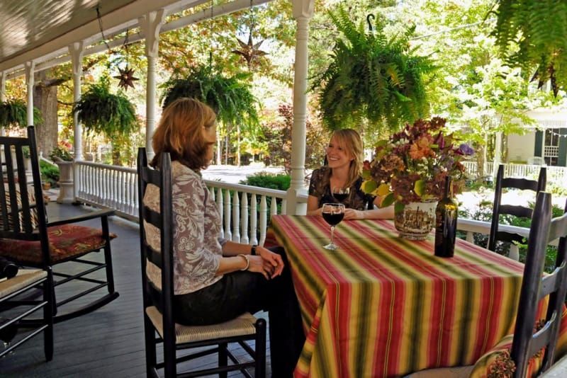 Two women are sitting at a table on a porch drinking wine.