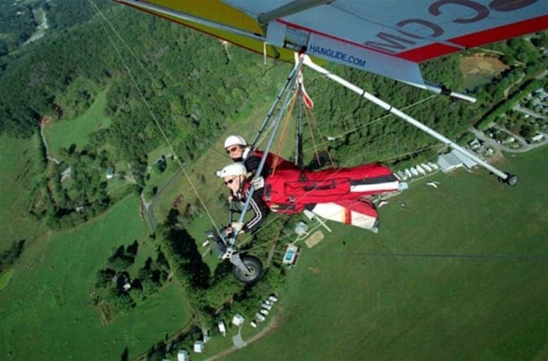 Two people are flying in a hang glider with the letters cc on the wing
