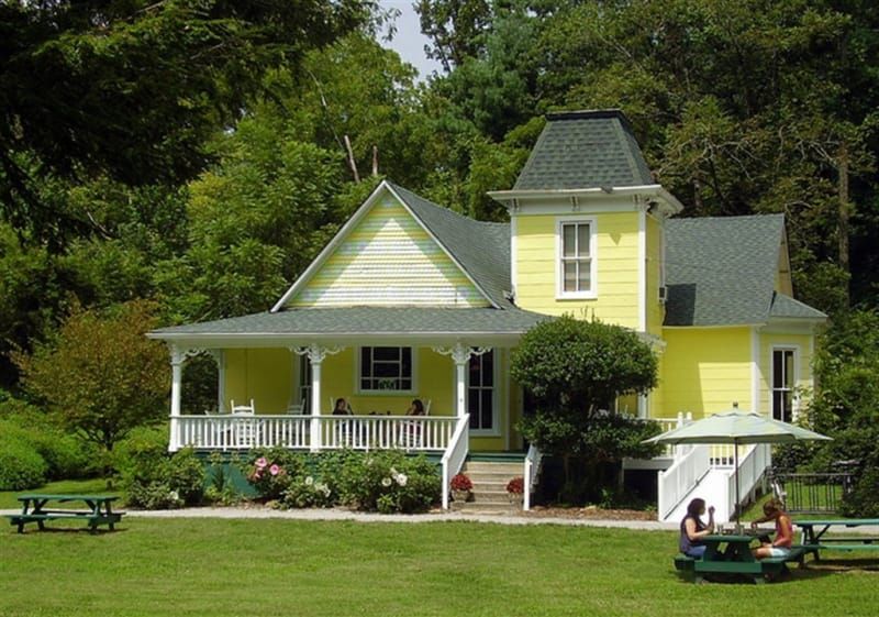 A yellow house with people sitting at picnic tables in front of it