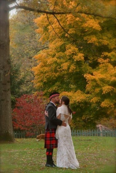 A bride and groom are kissing in front of a tree in a park.