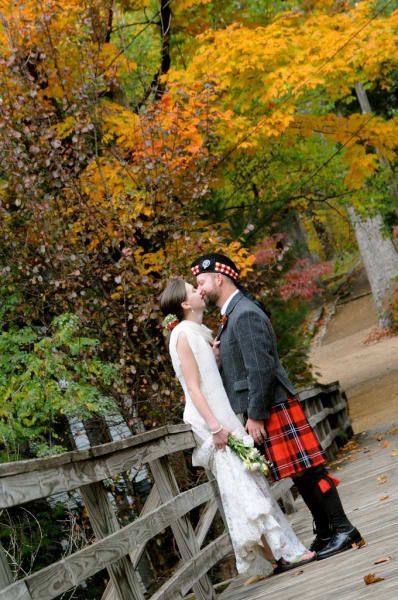 A bride and groom are kissing on a wooden bridge . the bride is wearing a kilt.