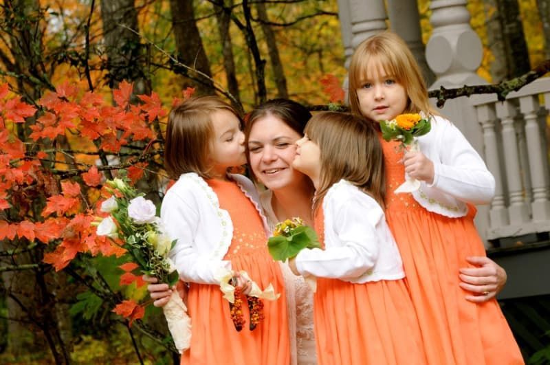 A woman is kissed on the cheek by two flower girls