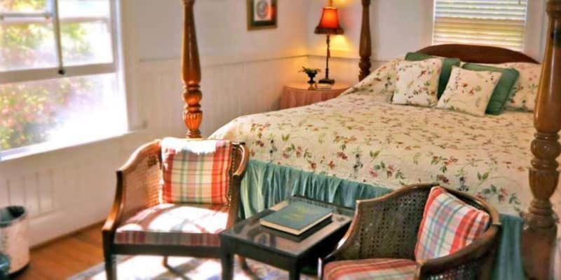 A bedroom with a four poster bed , chairs , a table and a window.