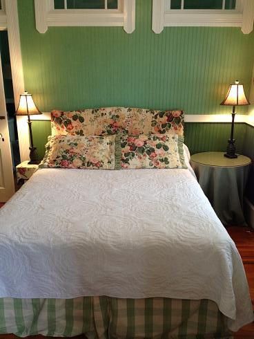 A bed with a white blanket and floral pillows in a bedroom with green walls.