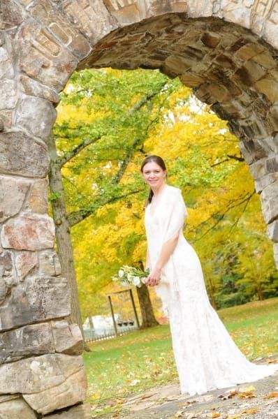 A woman in a wedding dress is standing under an archway holding a bouquet of flowers.