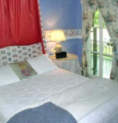 A bedroom with a bed , nightstand , lamp and window.