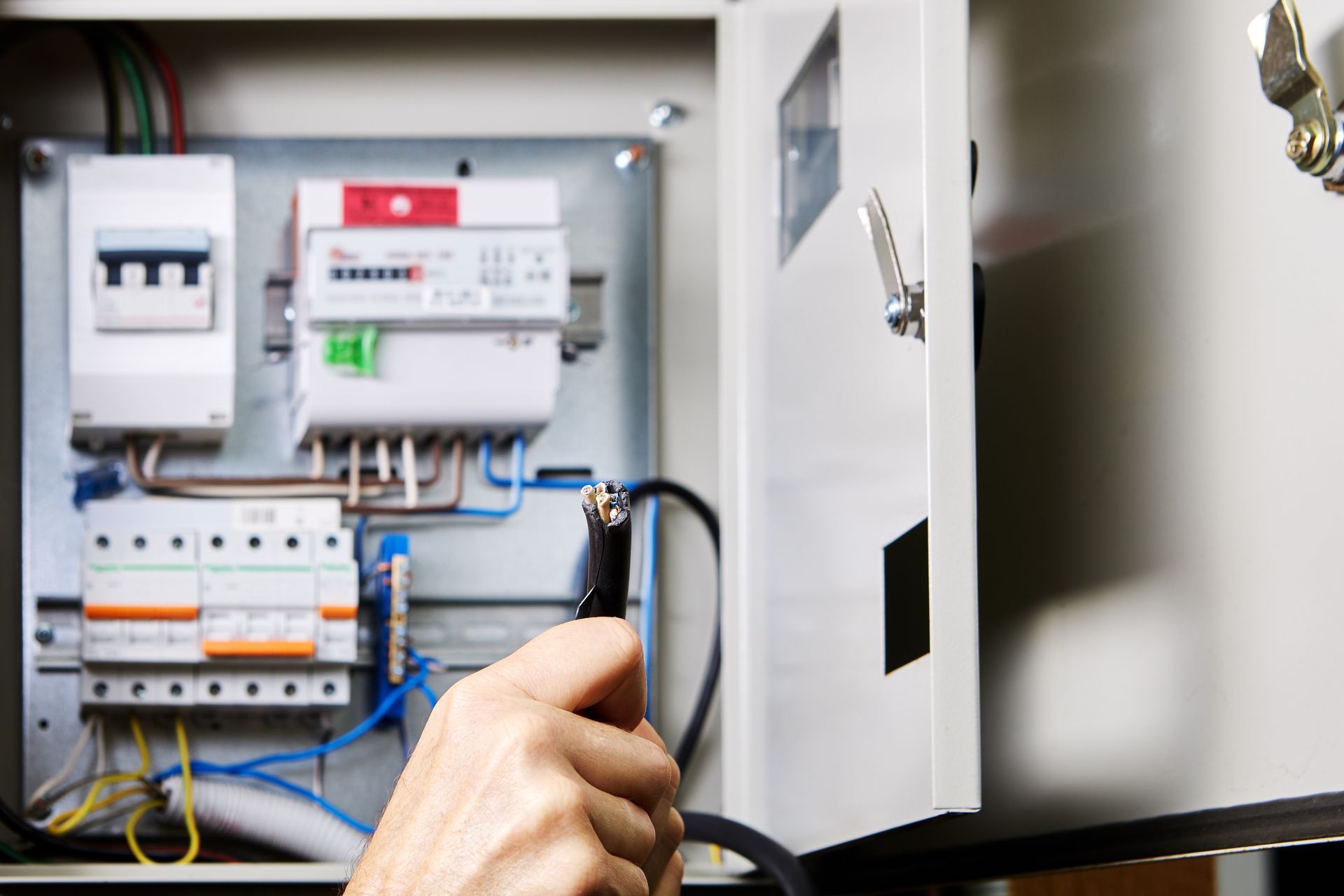 Electrician working on electrical panel, wearing white shirt, indoors.