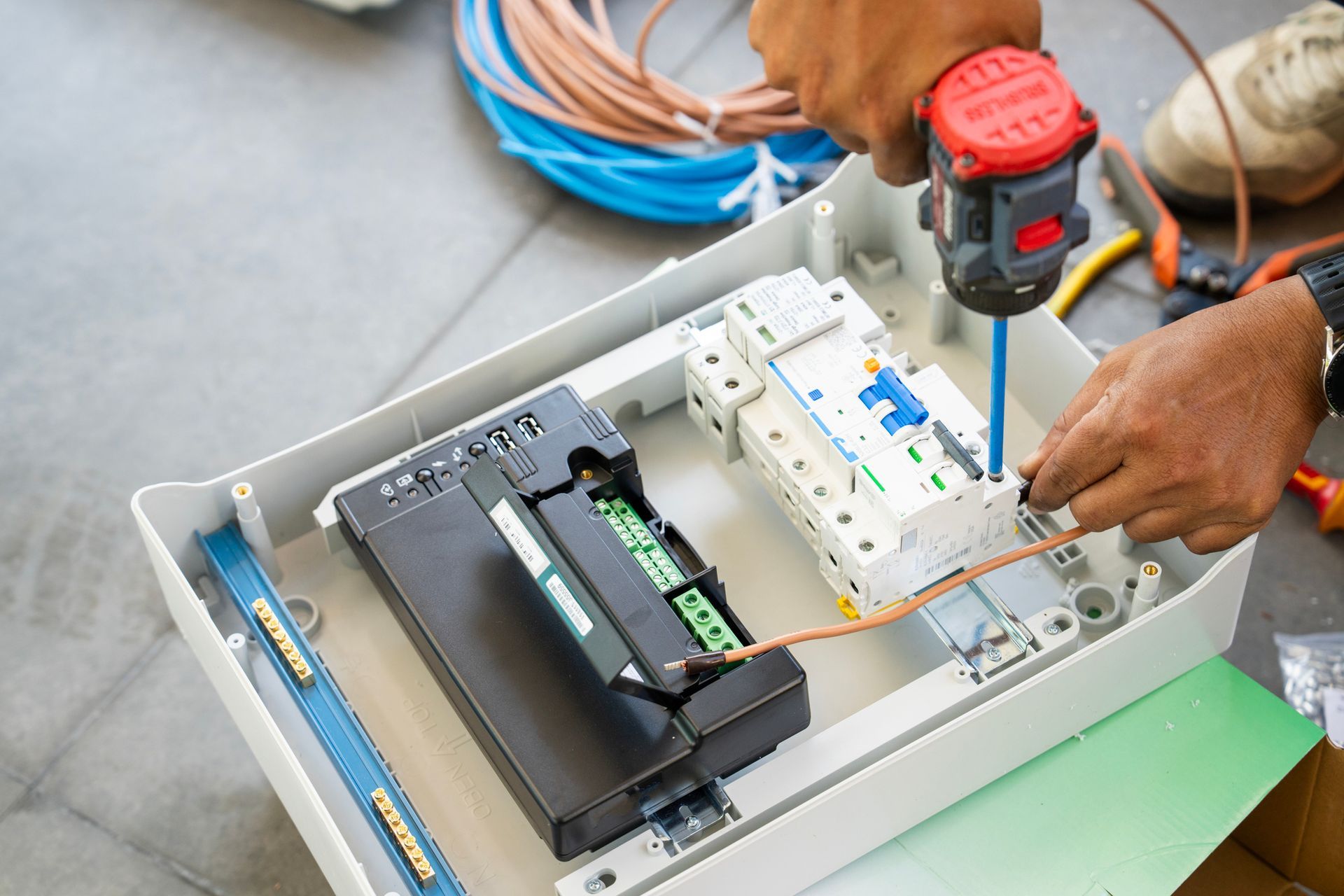 Electrician installing wiring in a white electrical box with a power drill.