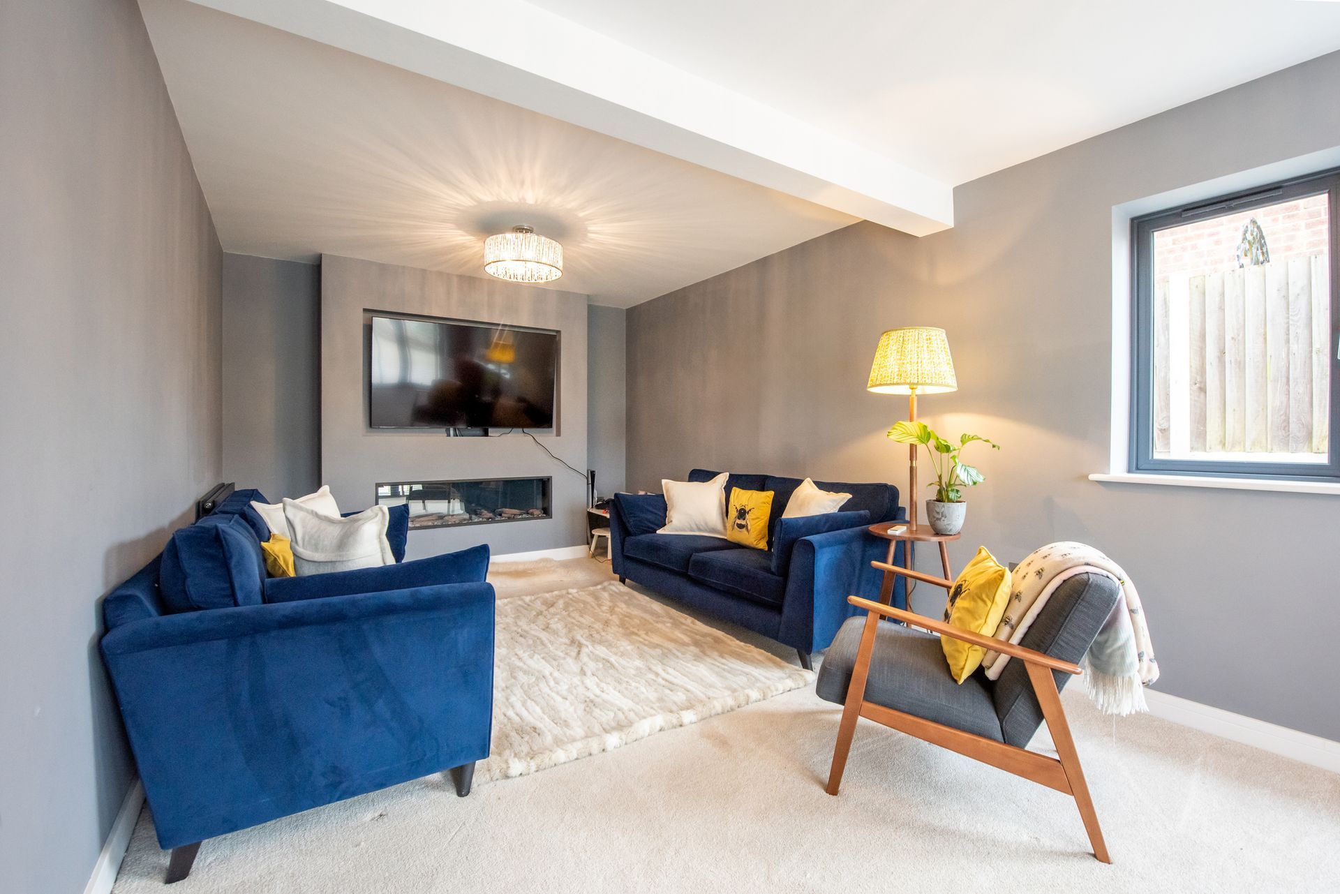 Cozy living room with blue sofas, a chair, and a rug. Gray walls and a television are visible.