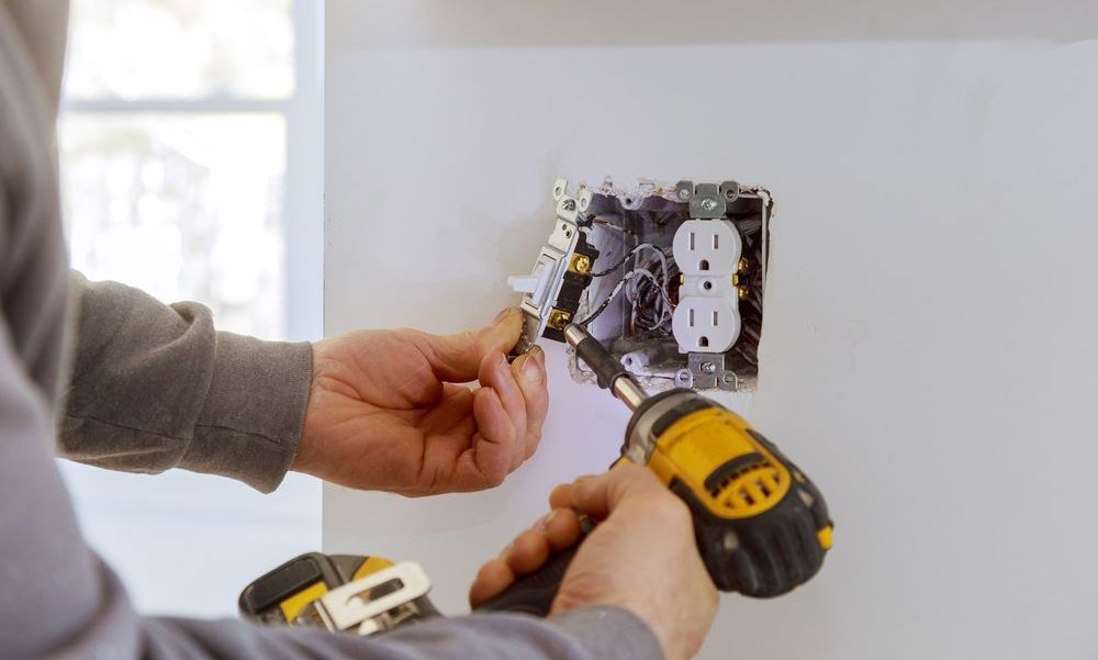 A man is installing an electrical outlet on a wall with a drill.