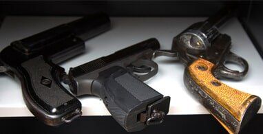 Three handguns are displayed on a white shelf. They have black and silver metal bodies, with dark grips, and are likely for storage.
