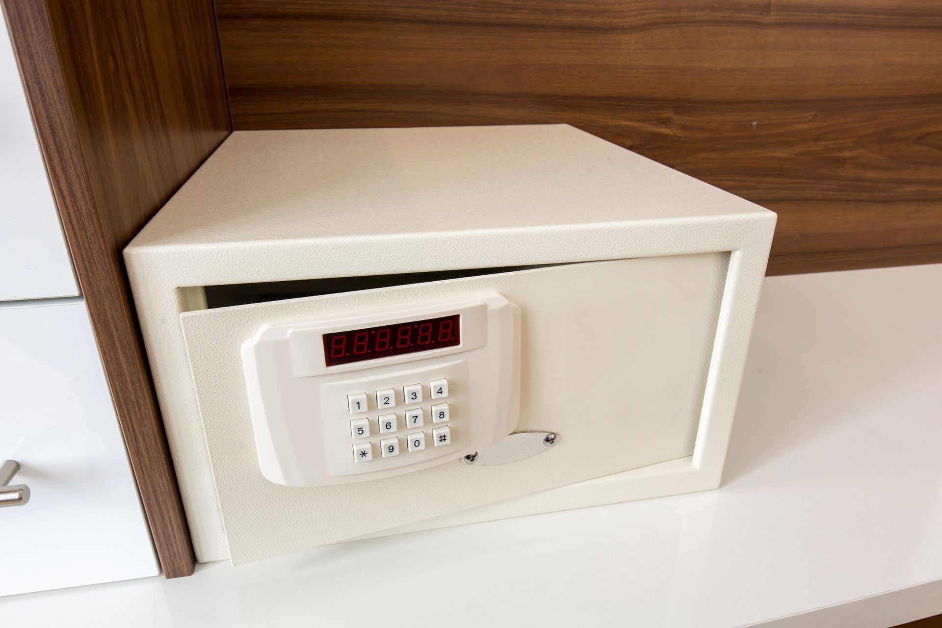 White electronic safe with digital keypad and LED display in wooden cabinet.