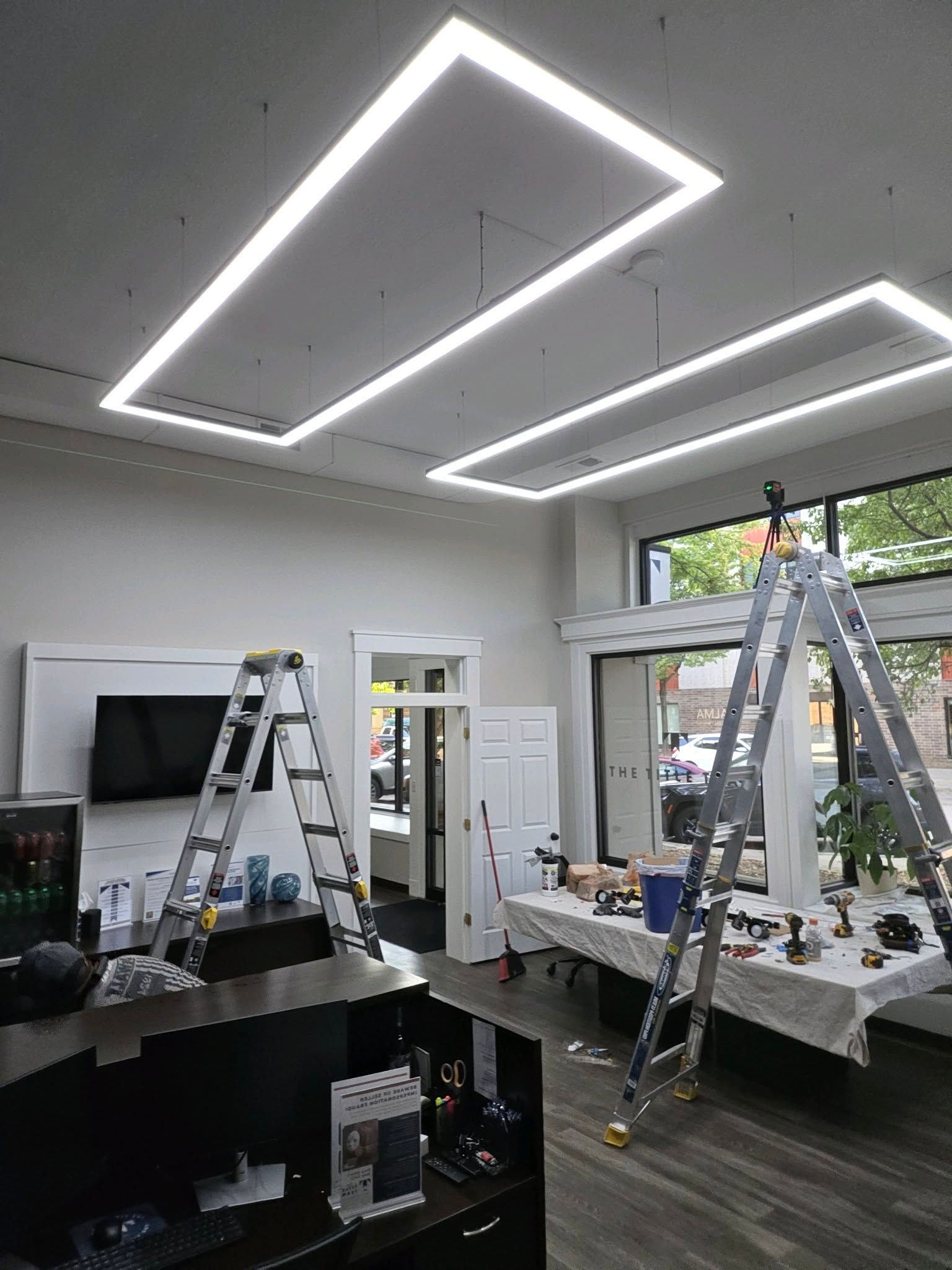 Bright office under construction with ladders, tools, and unfinished geometric ceiling lights
