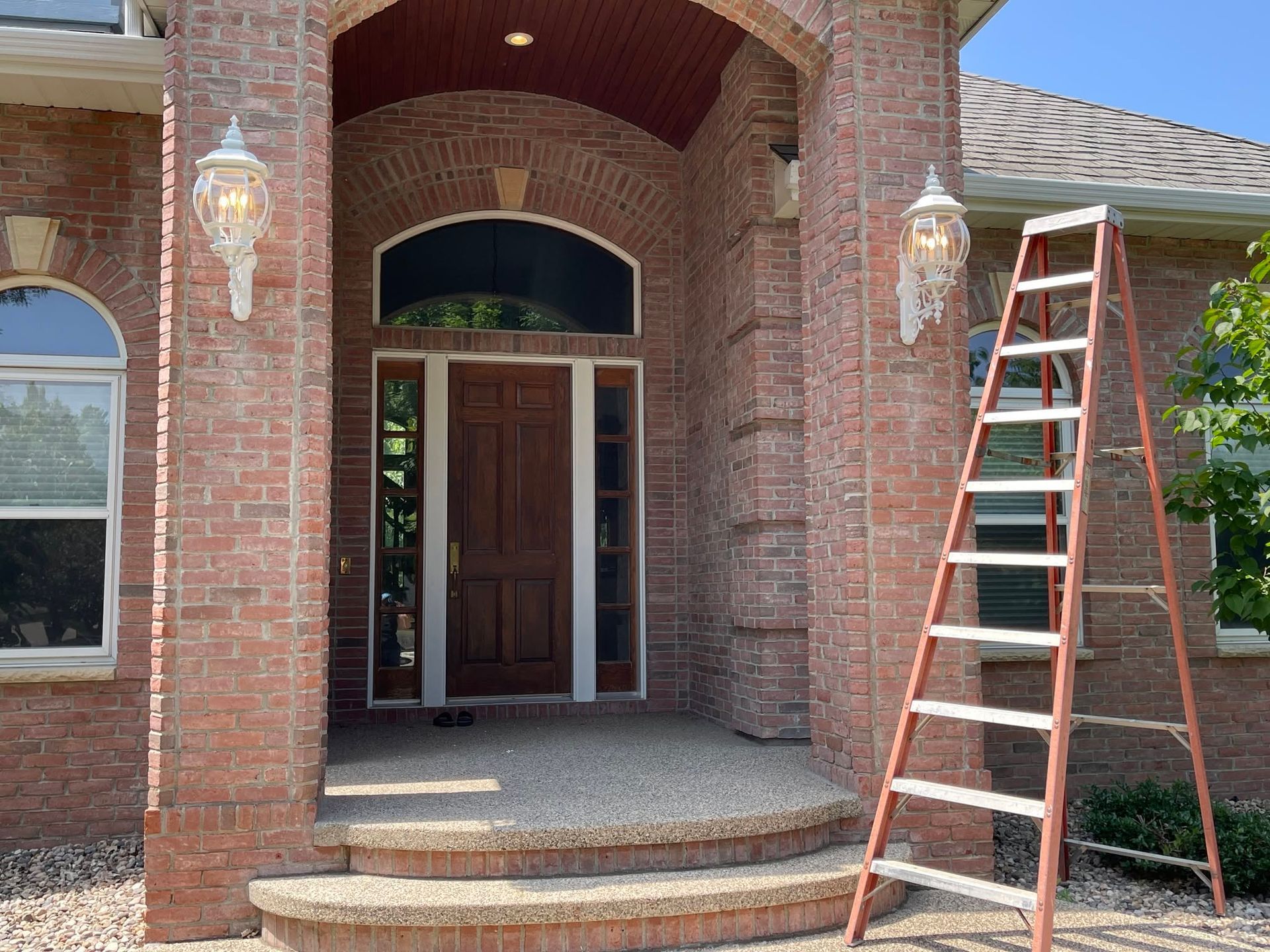 Brick house front entry with arched porch, double doors, and a ladder leaning on the right side