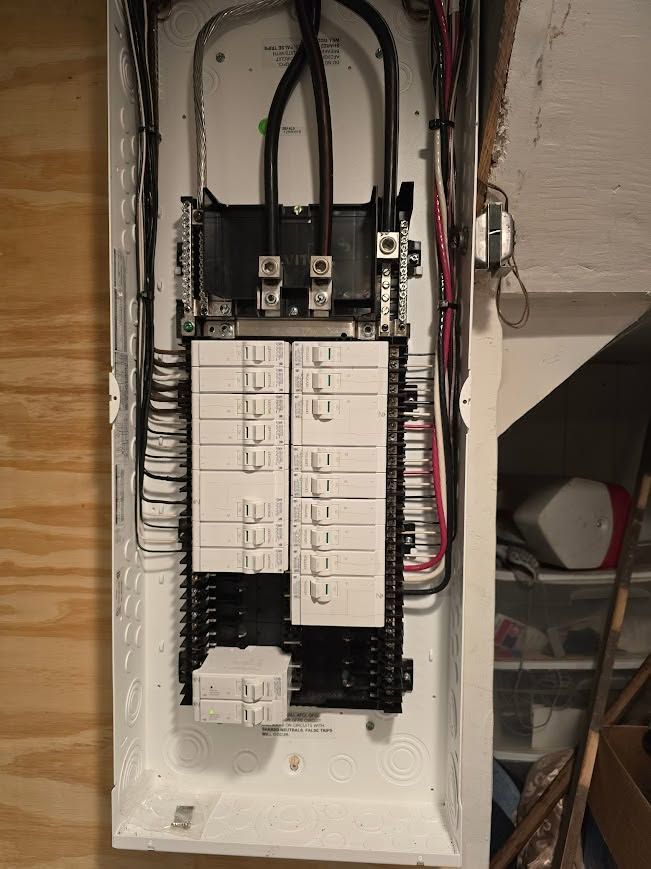 Open electrical breaker panel with white circuit breakers and exposed wiring in a wall recess