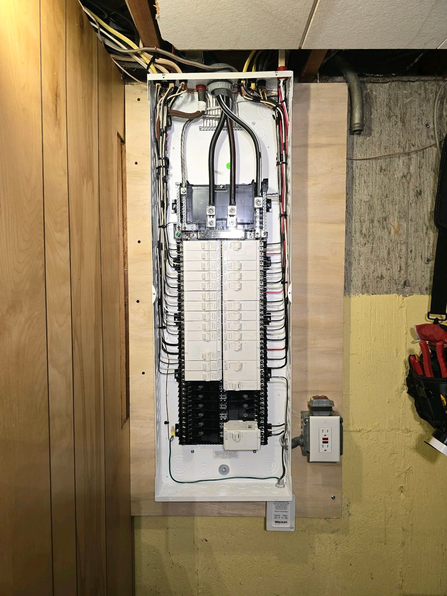 Open electrical breaker panel in basement wall, with wiring exposed and cover removed.