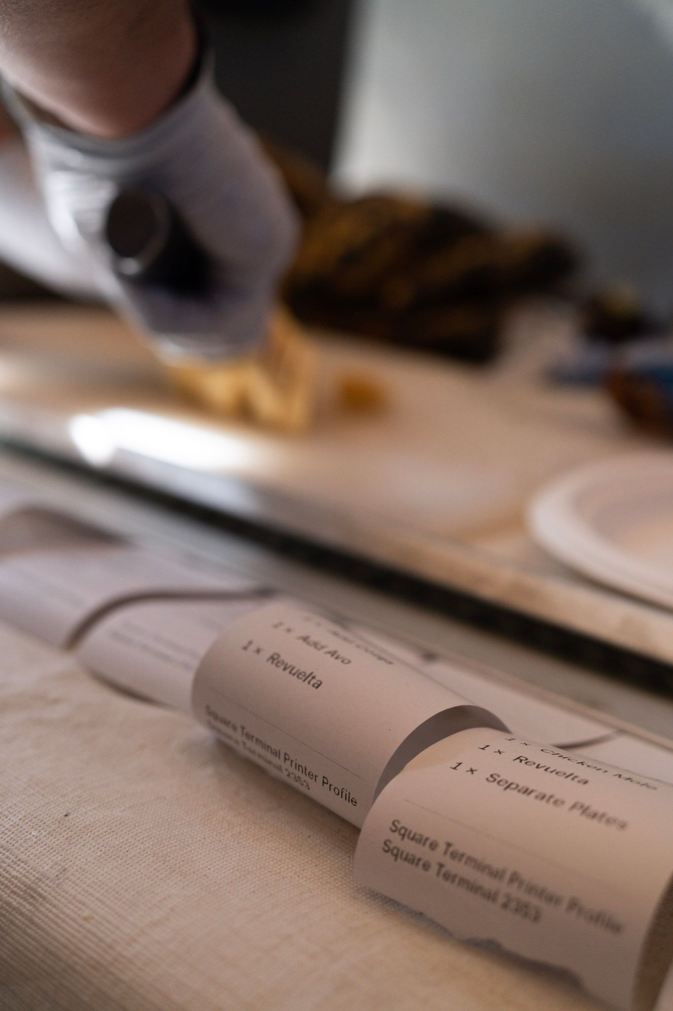 Person in gloves cuts food on a table near labeled paper rolls.