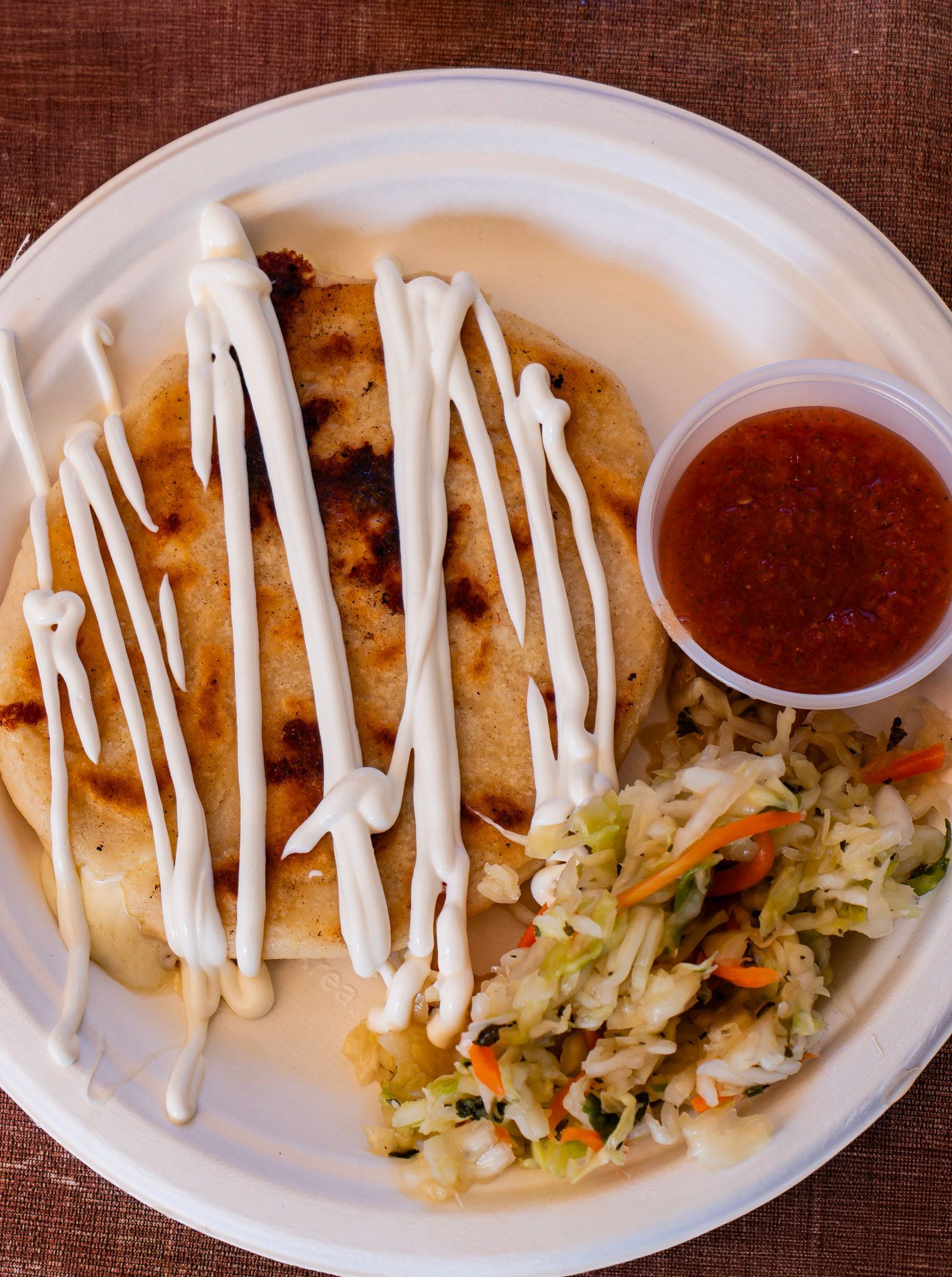 Pupusas drizzled with sauce, salsa, and slaw on a white plate.