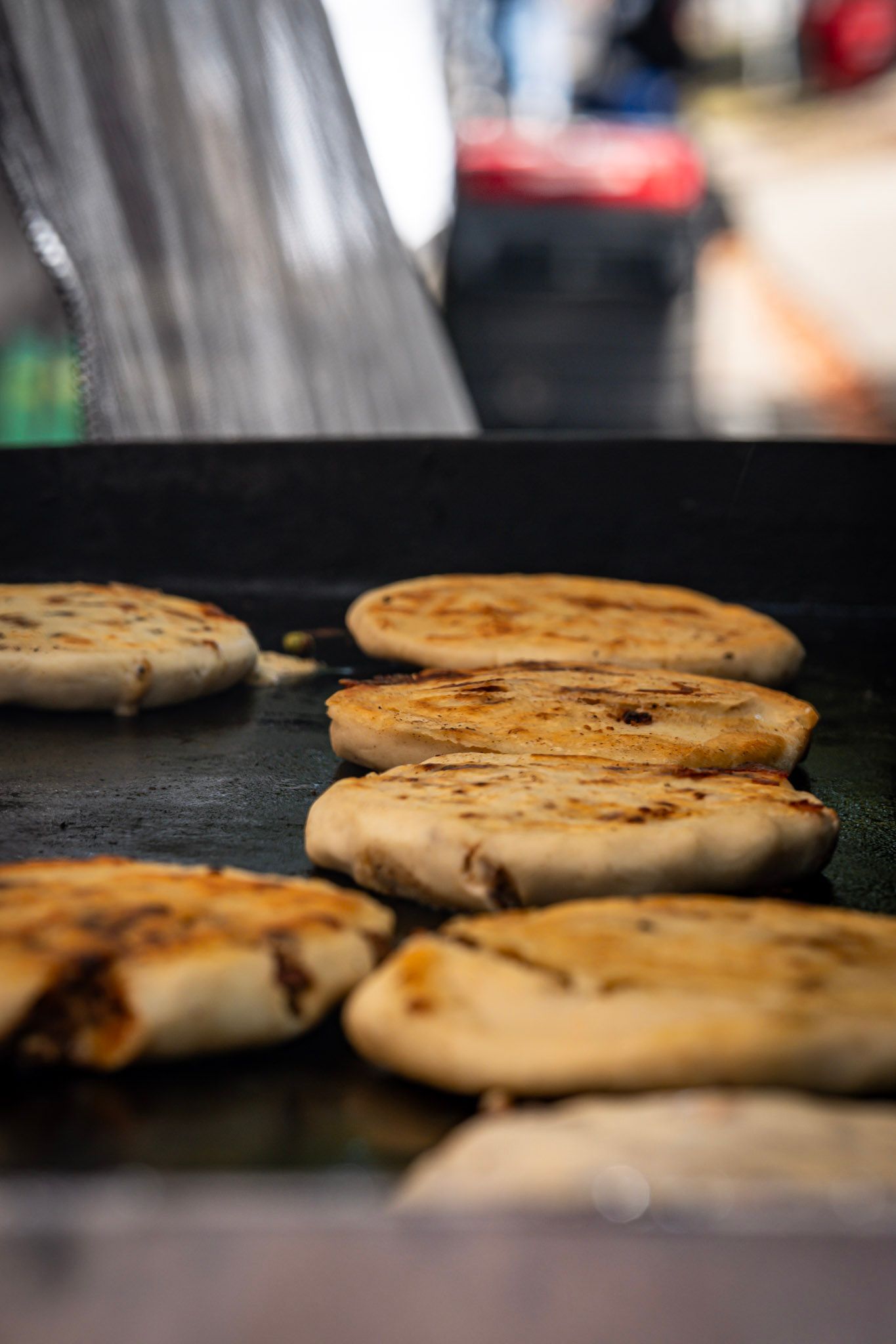 Flatbreads grilling on a hot griddle, browning with visible fillings. Street food vendor.