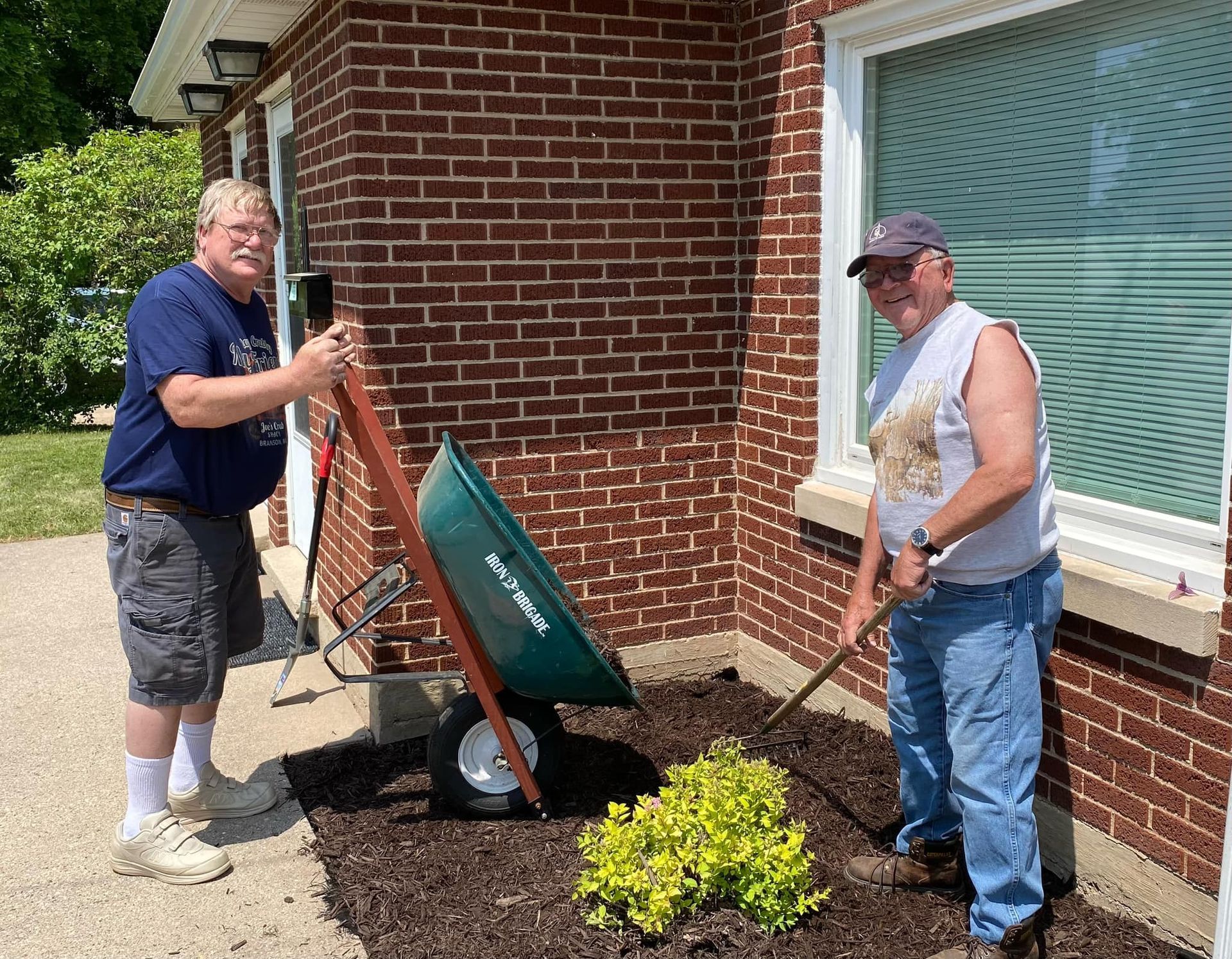 Two men are working in a garden with a wheelbarrow.