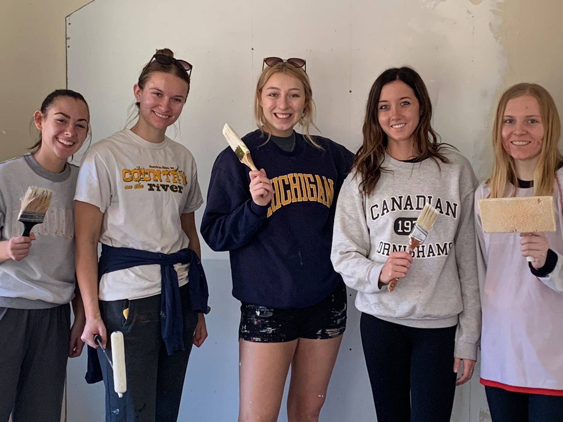 A group of young women are standing next to each other holding paint brushes.