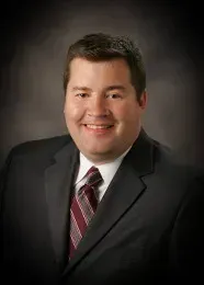 Man in suit smiling, with burgundy striped tie.