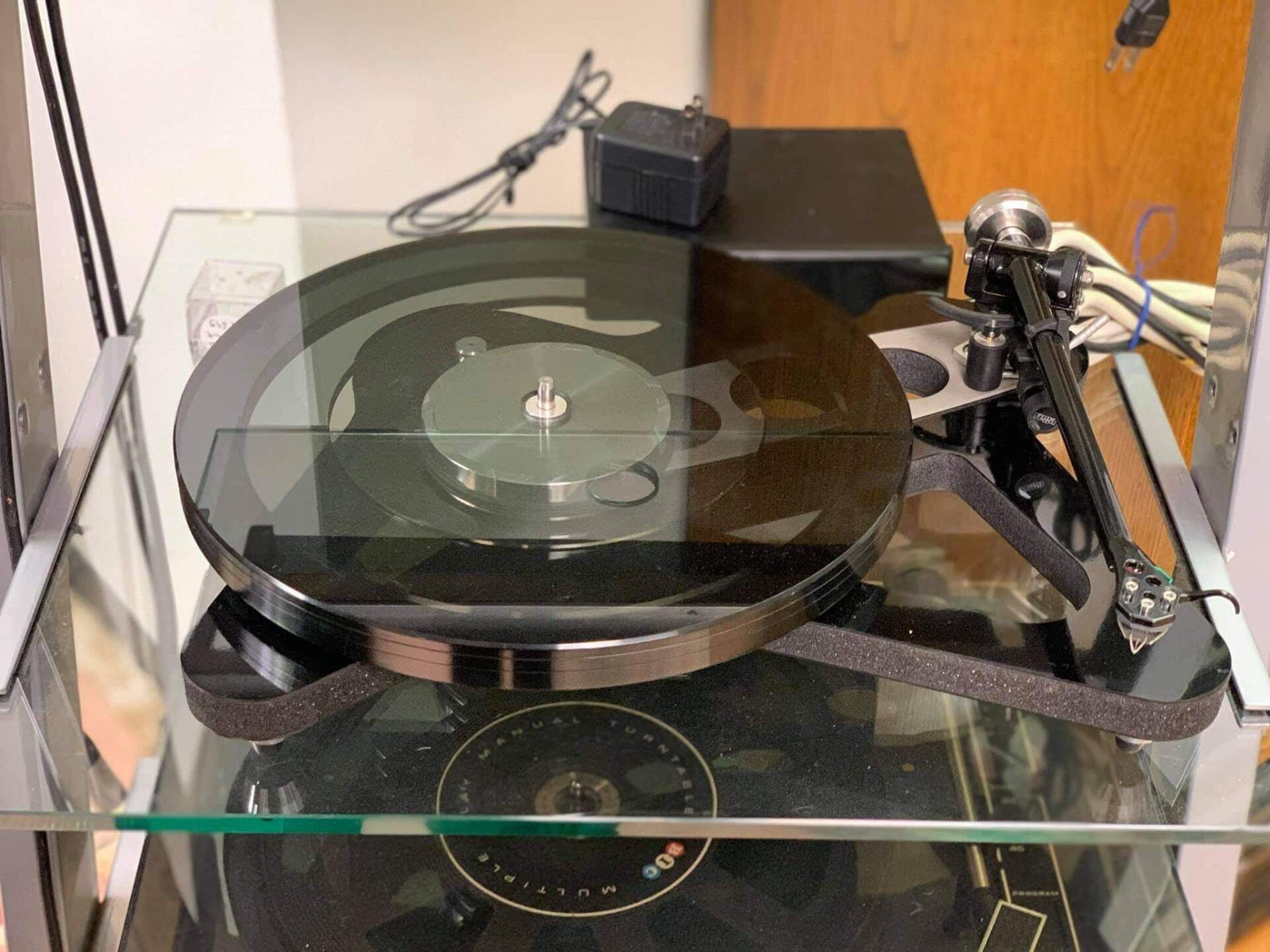 A record player is sitting on top of a glass shelf.