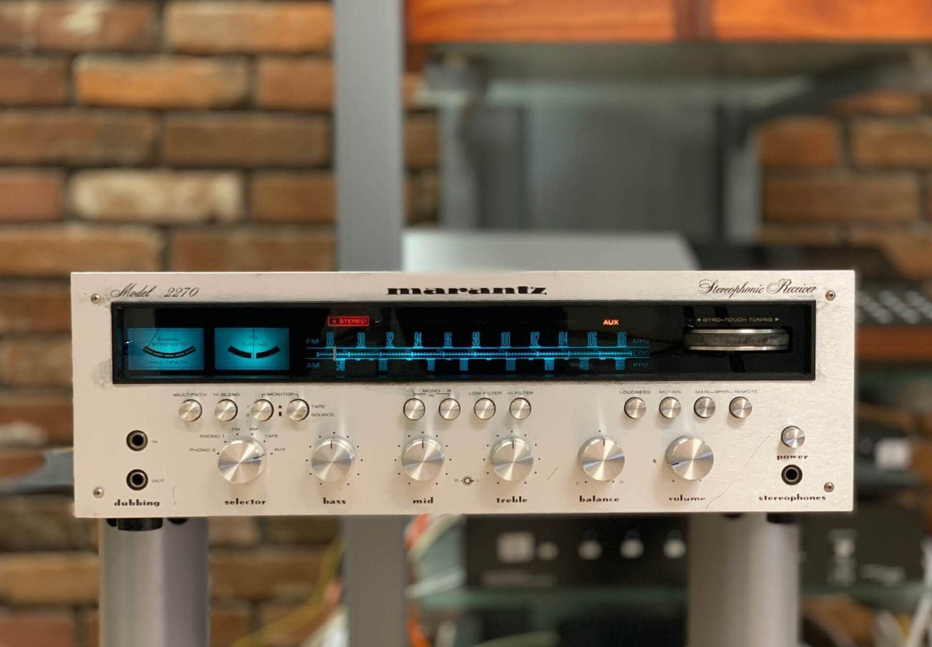 A stereo receiver is sitting on a stand in front of a brick wall.