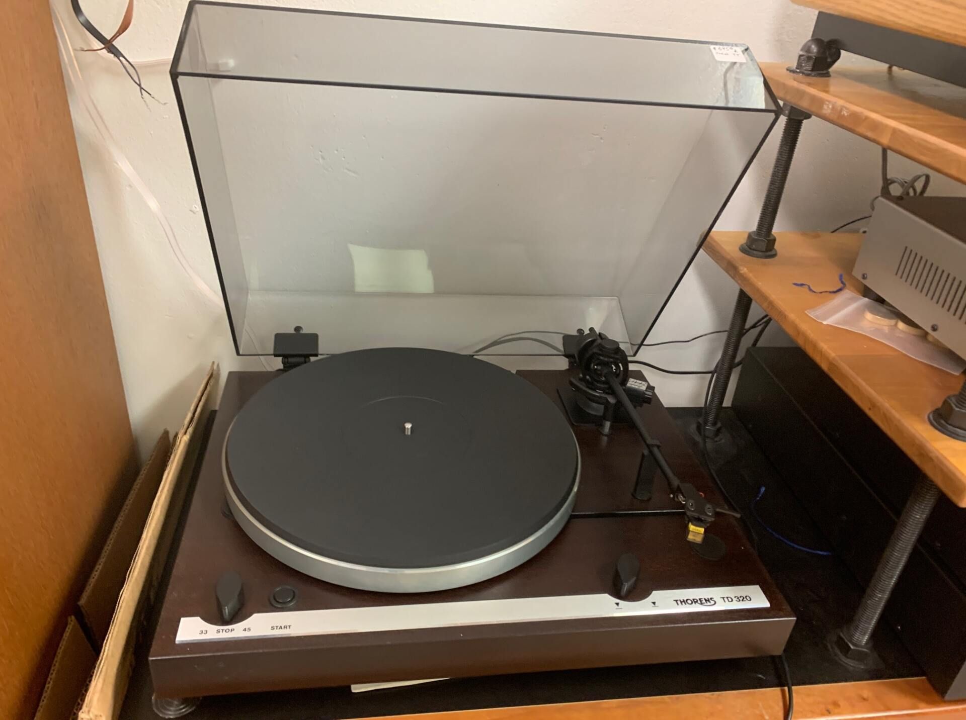 A record player is sitting on top of a wooden shelf.