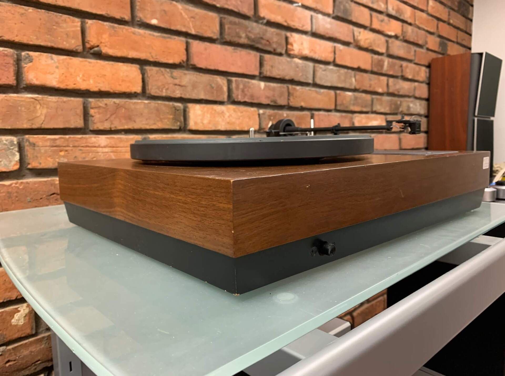 A record player is sitting on a glass table in front of a brick wall.