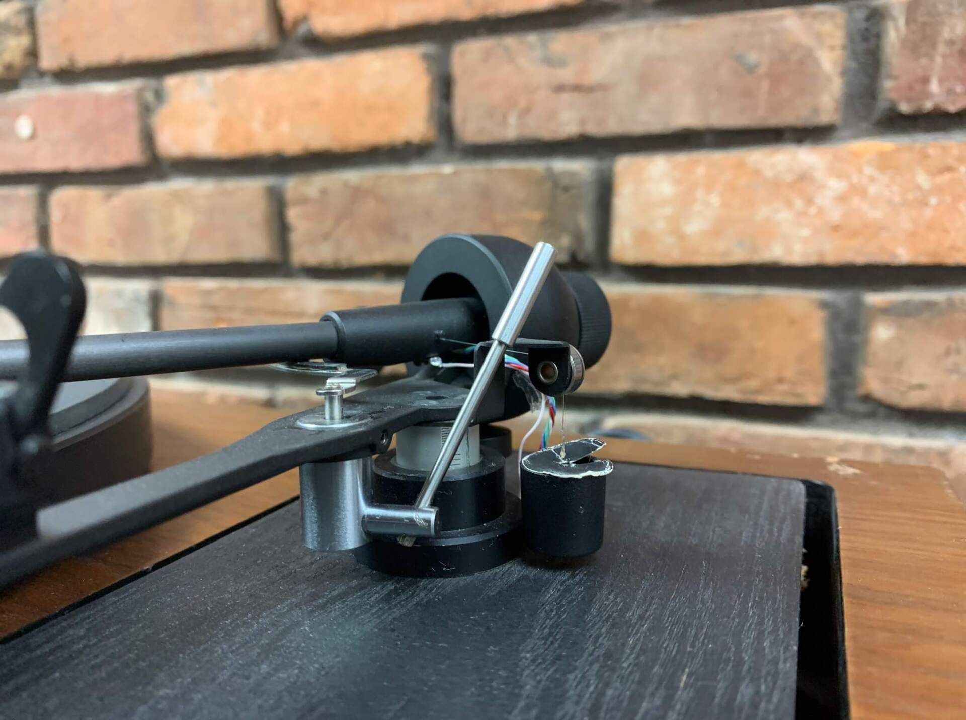 A record player is sitting on a wooden table in front of a brick wall.