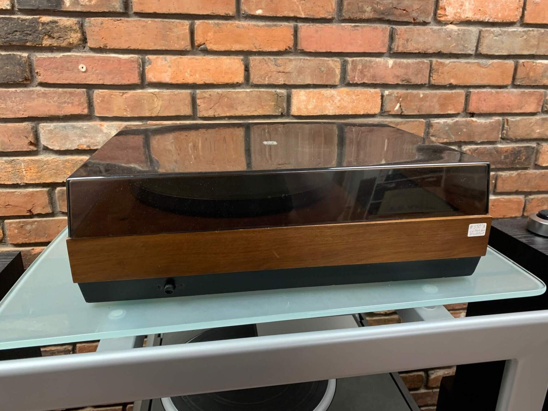 A record player is sitting on a glass table in front of a brick wall.