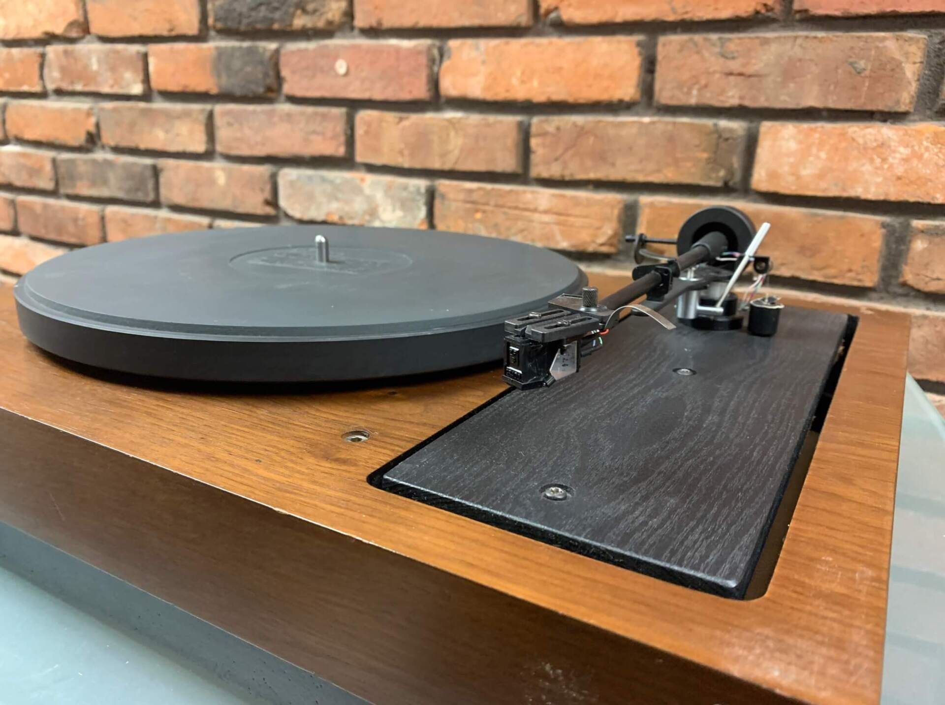 A record player is sitting on top of a wooden table in front of a brick wall.