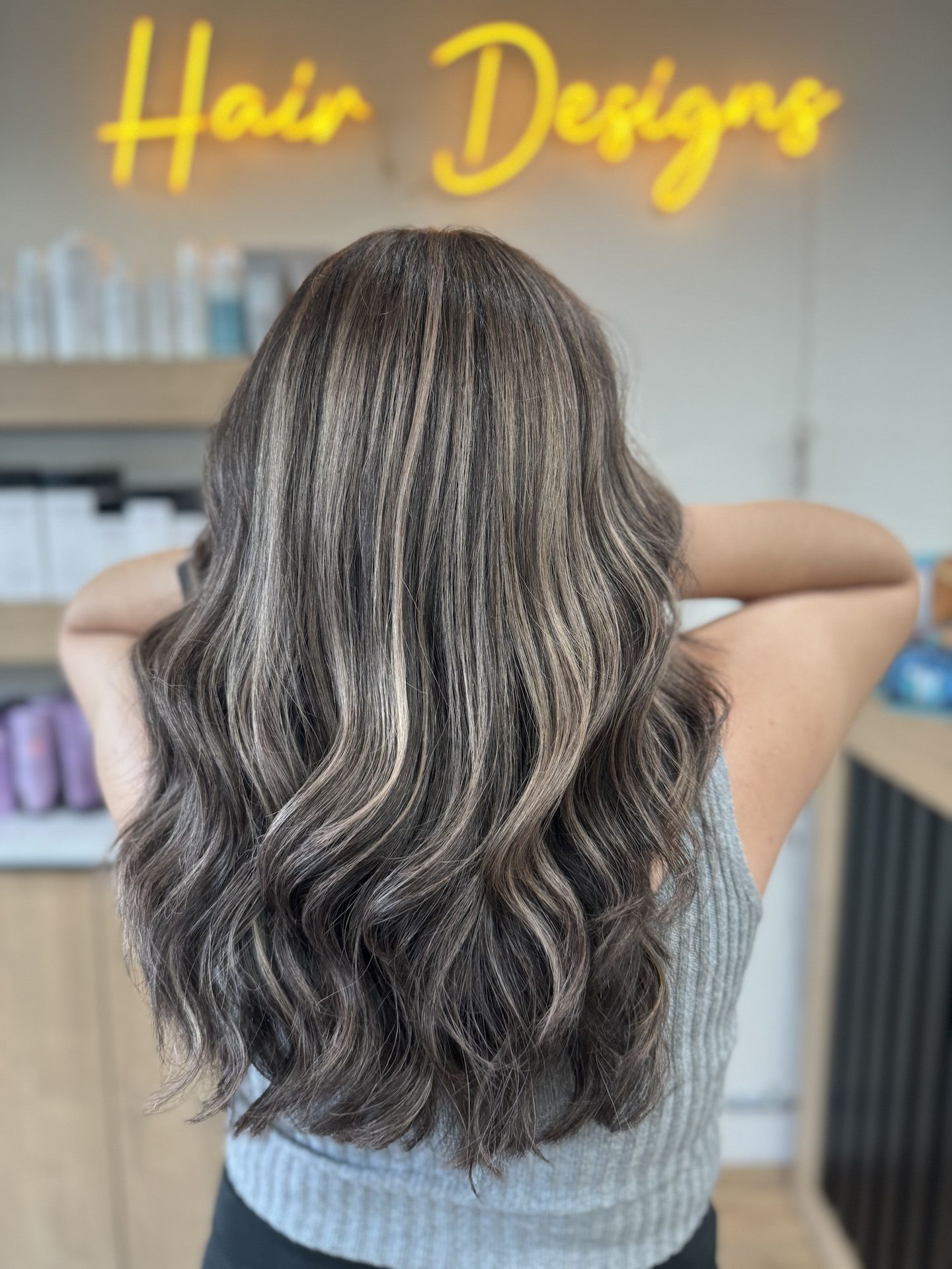 A woman is standing in front of a sign that says hair designs