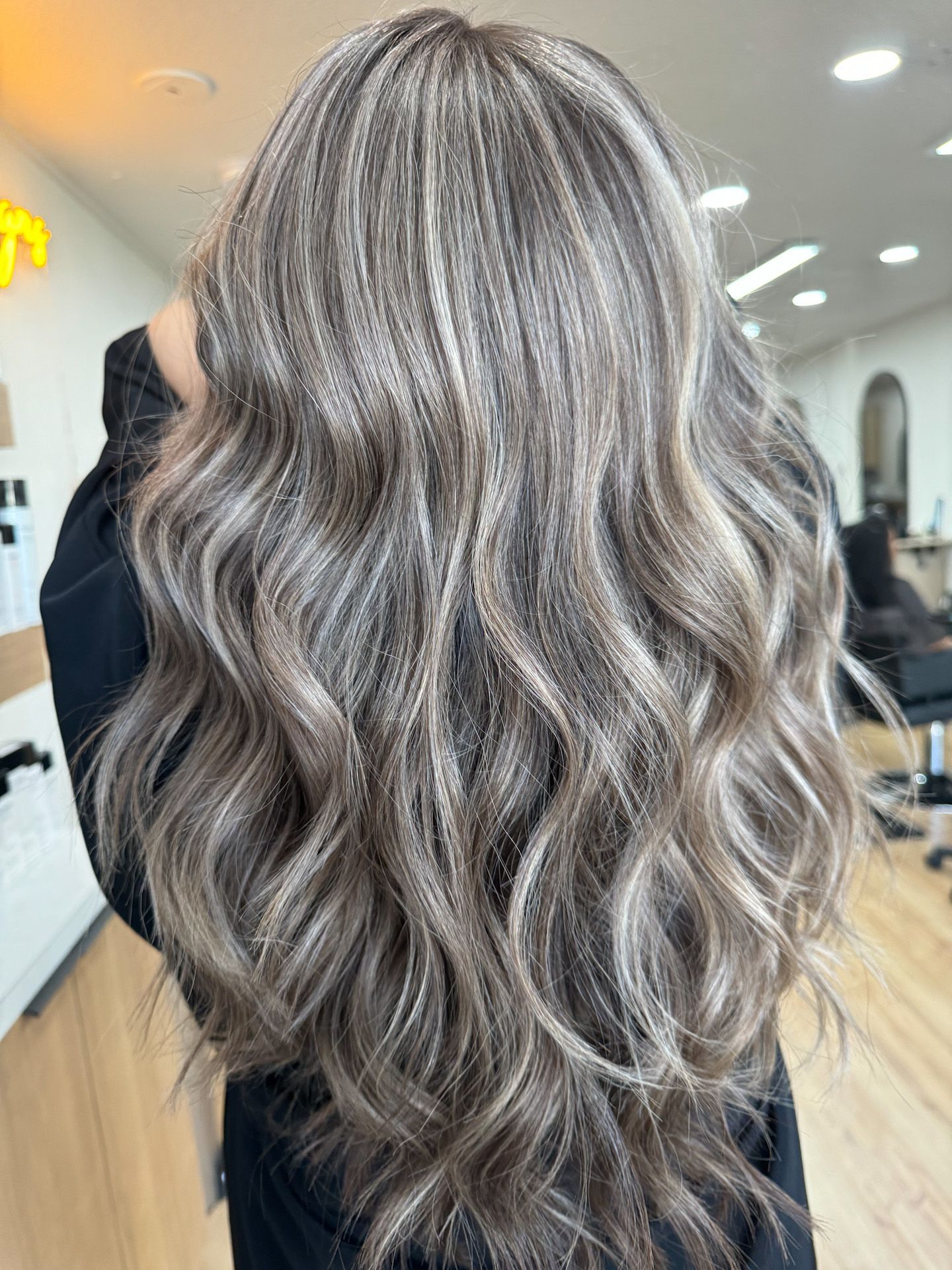A woman with long wavy hair is standing in a salon.