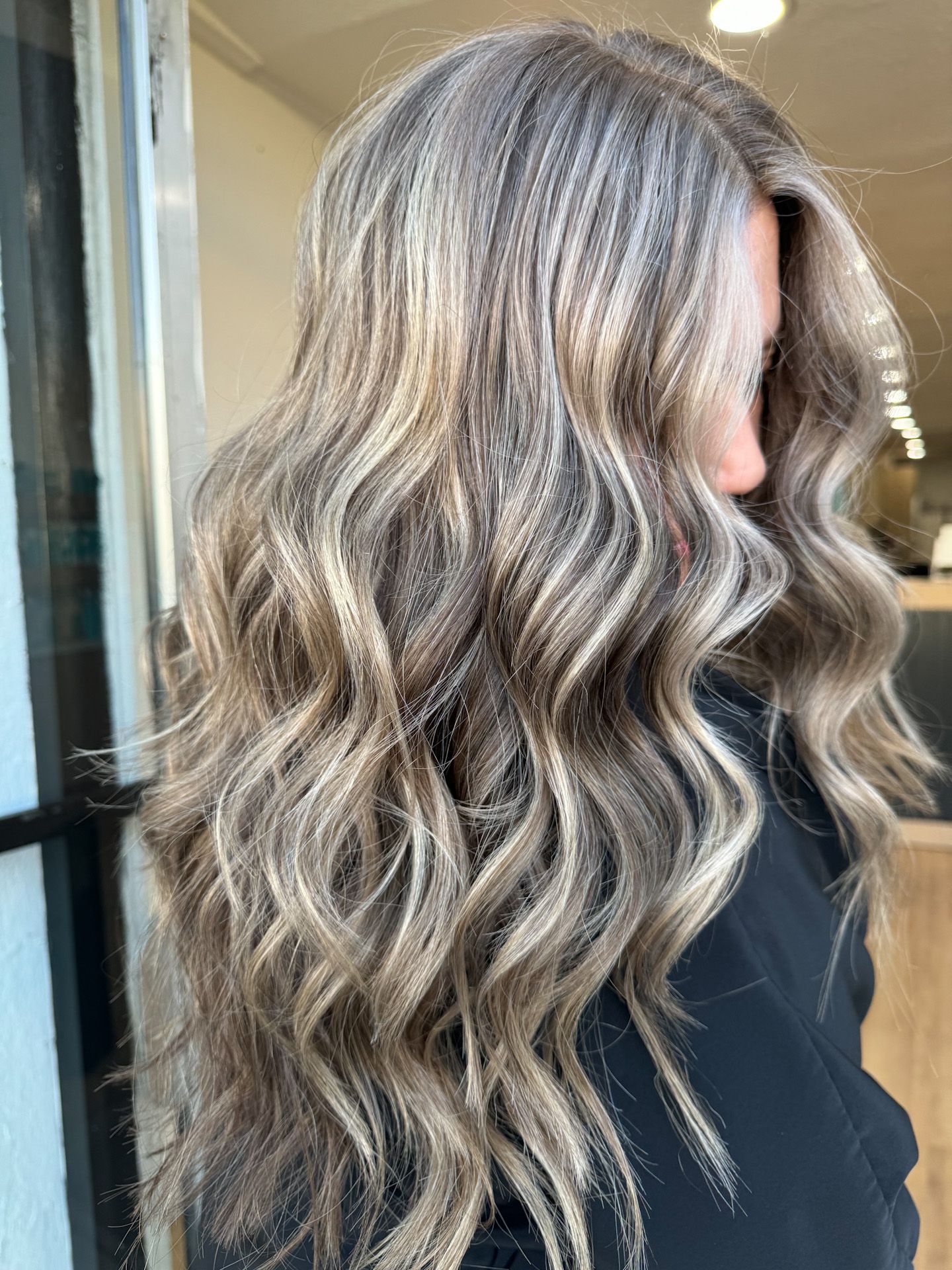 A woman with long wavy gray hair is standing in front of a window.