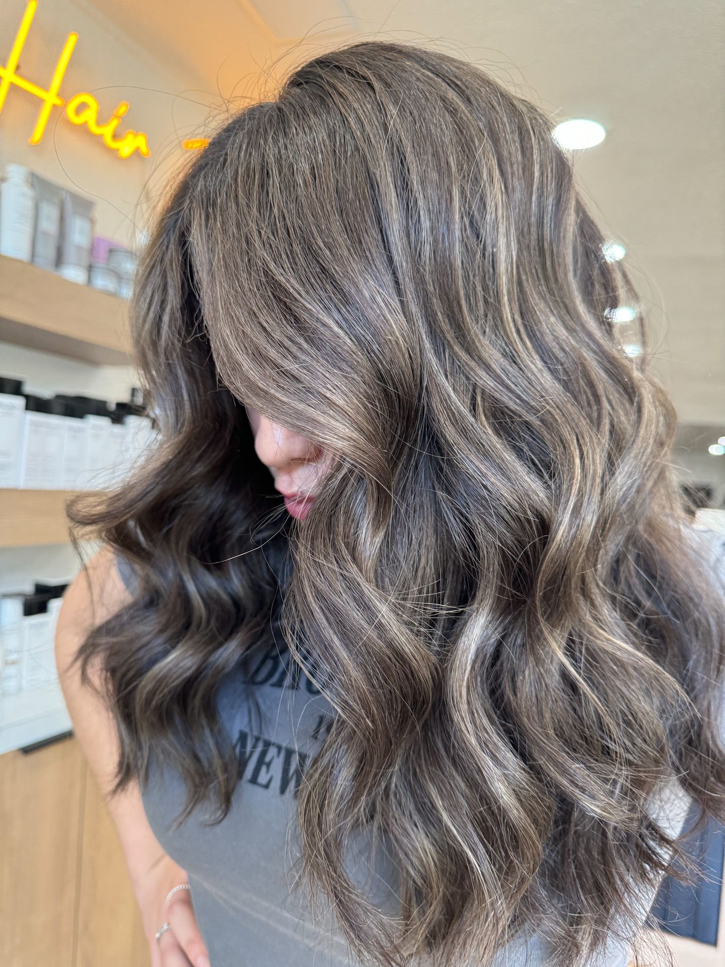 A woman with long brown hair is standing in a salon.