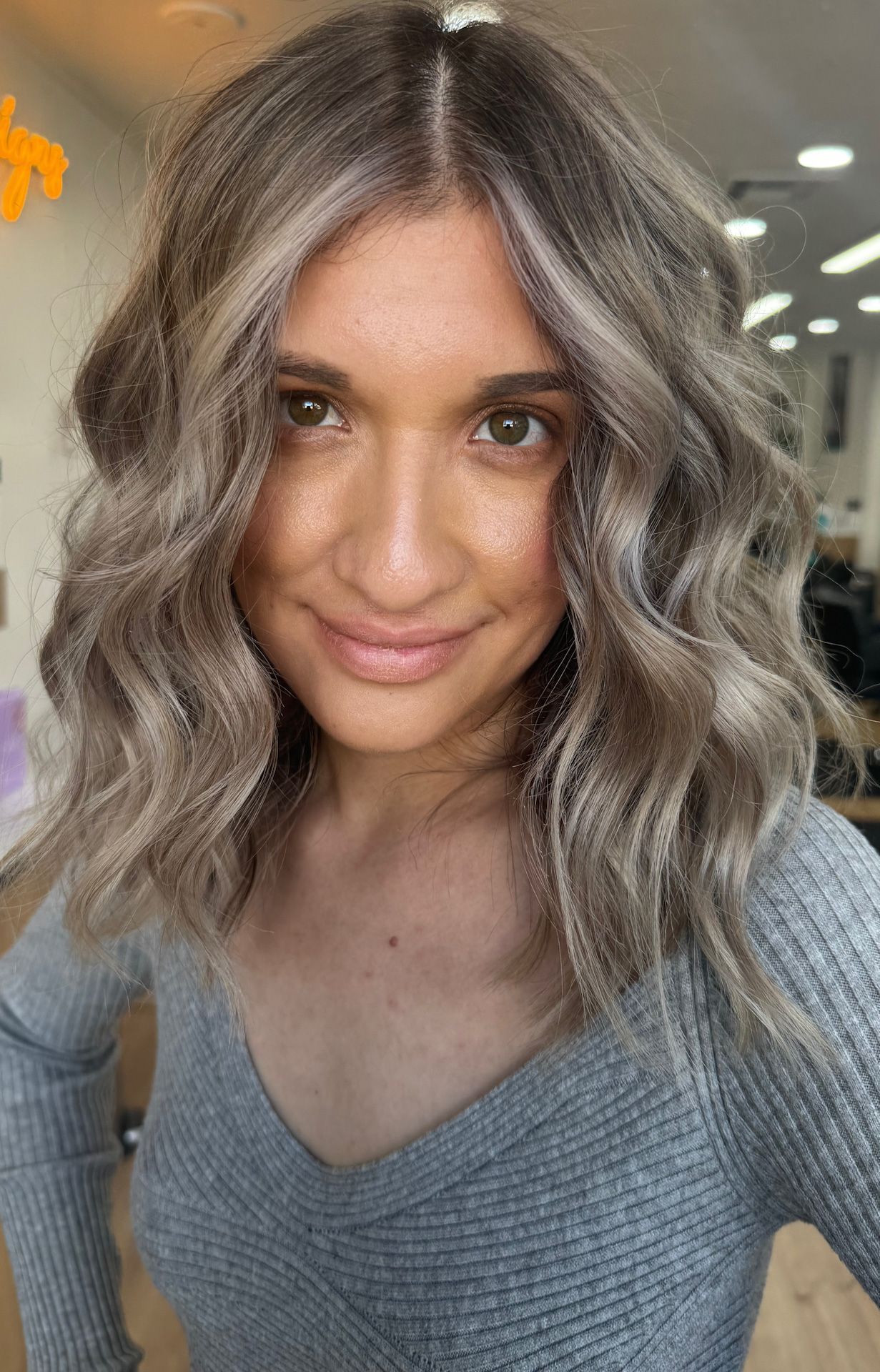 A woman with gray hair is wearing a gray sweater and smiling.